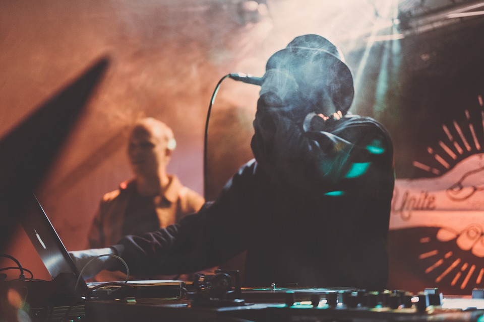 DJ mit Kapuze an den Turntables, stimmungsvolles Licht und Nebel im Hintergrund.