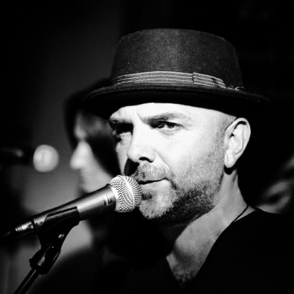 Sänger in Schwarz-Weiß mit Hut am Mikrofon, fokussierter Blick