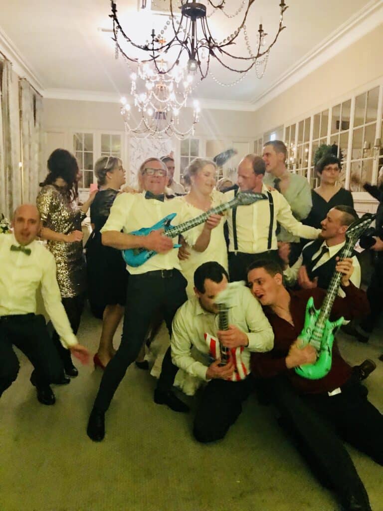 Fröhliche Hochzeitsgäste tanzen mit aufblasbaren Instrumenten unter einem Kronleuchter